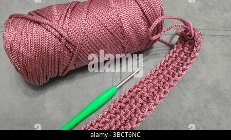 Stricken von Elementen einer rosafarbenen Damentasche, Handstricken mit langem Griff. Schritt-für-Schritt-Anweisungen. Auf grauem Hintergrund. Stockfoto