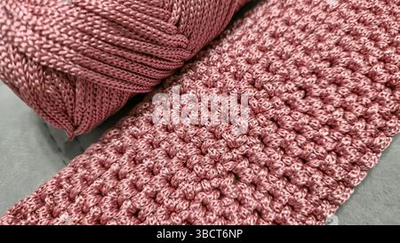 Stricken von Elementen einer rosafarbenen Damentasche, Handstricken mit langem Griff. Schritt-für-Schritt-Anweisungen. Auf grauem Hintergrund. Stockfoto