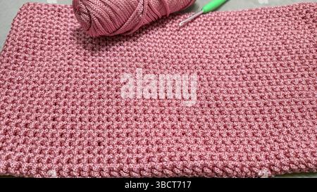 Stricken von Elementen einer rosafarbenen Damentasche, Handstricken mit langem Griff. Schritt-für-Schritt-Anweisungen. Auf grauem Hintergrund. Stockfoto