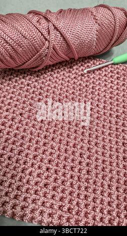 Stricken von Elementen einer rosafarbenen Damentasche, Handstricken mit langem Griff. Schritt-für-Schritt-Anweisungen. Auf grauem Hintergrund. Stockfoto