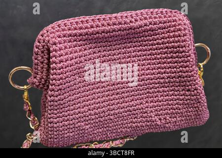 Pinke Damenhandtasche, handgestrickt, mit langem Griff. Details und Elemente. Auf grauem Hintergrund. Stockfoto