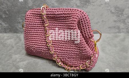 Pinke Damenhandtasche, handgestrickt, mit langem Griff. Details und Elemente. Auf grauem Hintergrund. Stockfoto