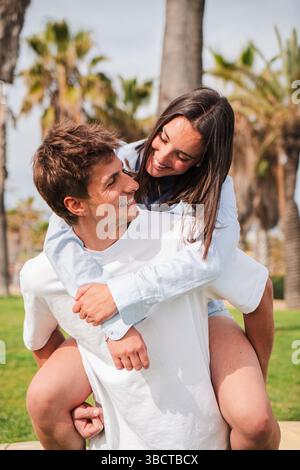 Ein fröhliches Paar genießt einen verspielten Moment bei einem Huckepack-Ritt, bei dem es lacht und Zuneigung teilt, während es sich gegenseitig in einer reizvollen Präsentation umgibt Stockfoto