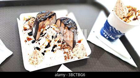 Semifreddo wird in zwei Hälften geschnitten, innen cremig, belegt mit Schokolade, Schlagsahne, Nüssen, und Karamellsauce, serviert mit Kaffee Stockfoto