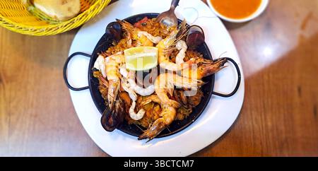 Traditionelle spanische Paella mit Meeresfrüchten, Reis und Zitrone, serviert in einer Pfanne auf einem Holztisch Stockfoto