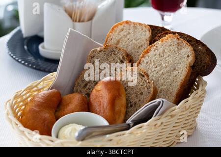 Brot im Korb. Weiß-schwarz geschnittenes Brot, Butter und Kuchen in einem Korb auf dem Tisch im Restaurant Stockfoto