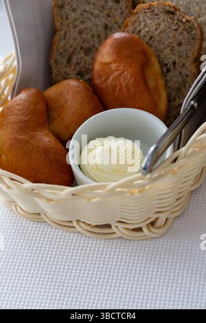 Brot im Korb. Weiß-schwarz geschnittenes Brot, Butter und Kuchen in einem Korb auf dem Tisch im Restaurant Stockfoto