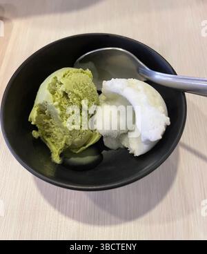 Erfrischende Schaufeln grüner Tee und Kokos-Eis in einer schwarzen Schüssel – eine unwiderstehliche Mischung aus cremiger Textur und exotischen Aromen bei jedem Happen. Stockfoto
