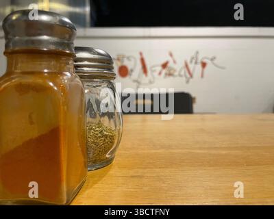Zwei Gewürzgläser aus Glas ruhen auf einem rustikalen Holztisch, elegante Küchenutensilien, die jedem kulinarischen Raum Geschmack, Funktion und ästhetischen Charme verleihen. Stockfoto