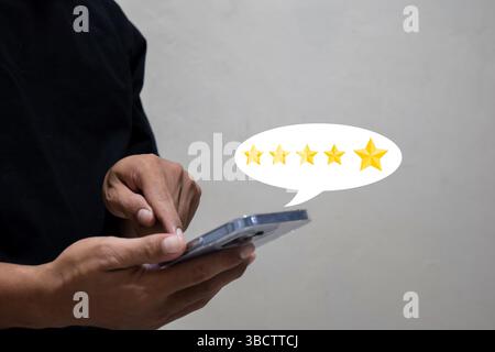 Der Kundenmann drückt mit der Hand auf den Smartphone-Bildschirm mit dem goldenen 5-Sterne-Feedback-Symbol und gibt den besten Punktepunkt für die Bewertung des Services an Stockfoto