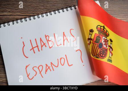 Konzept der mit Frage hablas espanol schreiben auf Buch und Flagge spaniens isoliert auf Holztisch. Stockfoto