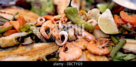 Köstlicher gegrillter Fisch und Meeresfrüchte wird mit frischem Gemüse und einer Limette garniert Stockfoto