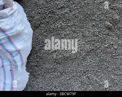 Nahaufnahme eines weißen gewebten Polypropylensacks, der auf einem Haufen trockengrauer Zementmischung oder Sand liegt und für Bau- und Pflasterarbeiten verwendet wird. Keine Personen. Stockfoto