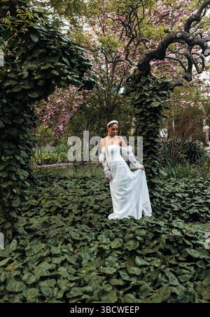 Die wunderschöne Braut im Spitzenkleid lächelt vor dem Hintergrund der Natur und der grünen Bäume Stockfoto