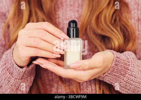 Frau, die kosmetisches Serum hält. Hände mit hellrosa Maniküre. Glasflasche mit Tropfverschluss. Hautpflege-Routinekonzept. Natürliche Schönheitsbehandlung. Stockfoto