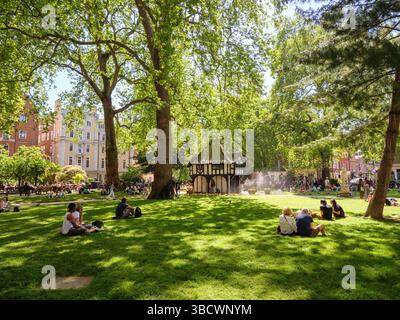Menschen, die im Schatten sitzen, in Soho Square Gardens, West End, Westminster, London, Großbritannien Stockfoto
