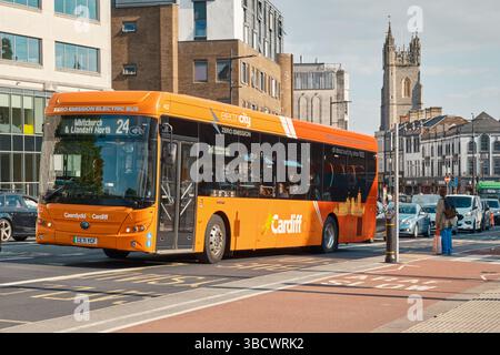 Cardiff Elektrobus auf der Route 24 nach Whitchurch und Llandaff North. Leuchtend orangefarbenes emissionsfreies Fahrzeug, das an einem sonnigen Tag durch das Stadtzentrum fährt. Stockfoto