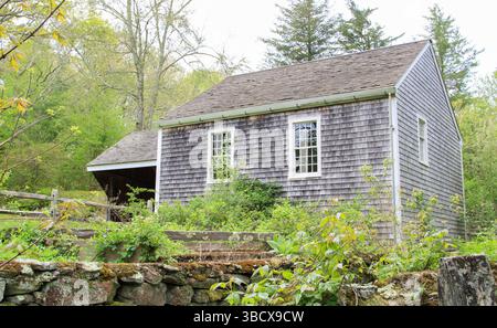Historisches New England Cape Home aus den 1700er Jahren mit braunem Schindelholzzaun und Steinmauer Stockfoto