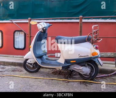 Kopenhagen, Dänemark - 9. März 2025: Ein geparkter weißer Roller mit schwarzem Sitz, neben einem roten Boot. Der Roller verfügt über eine hintere Zahnstange und ist Stockfoto