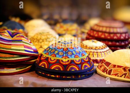 Farbenfrohe gestickte Kippahs (Yarmulkes), die an einem Marktstand aus dem Nahen Osten ausgestellt werden, zeigen komplexe traditionelle Textilhandwerkskunst. Stockfoto