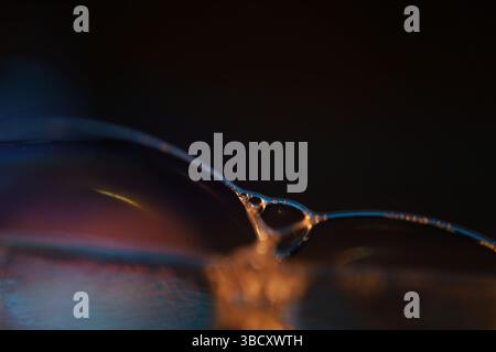 Makro aus Seifenblasenrand mit blauem und goldenem Licht und schillernden Oberflächendetails Stockfoto