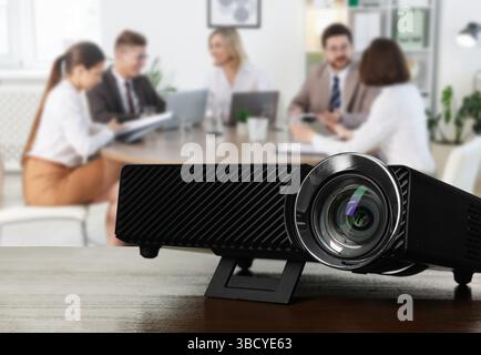 Moderner Videoprojektor auf Holztisch und Personen, die im Konferenzraum arbeiten, selektiver Fokus Stockfoto