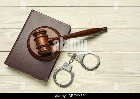 Handschellen mit Richtergabel und Gesetzbuch auf weißem hölzernem Hintergrund Stockfoto