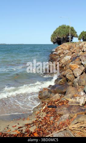 Meereswellen, die an einem Strand im Spinnaker Park in Gladstone, Queensland, Australien, auf Felsen und Sand abgespült werden Stockfoto
