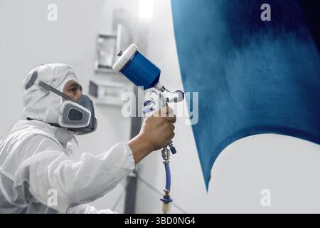Professioneller männlicher Autolackierer sprüht Autoteile in der Garage mit dem Airbrush auf blaue Farbe. Der Mann arbeitet mit der Spritzpistole. Stockfoto