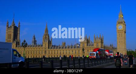 Houses of Parliament und Big Ben auf der Westminster Bridge mit blauem Himmel, roten Bussen, Verkehr und Menschen, die am frühen Morgen laufen. Stockfoto