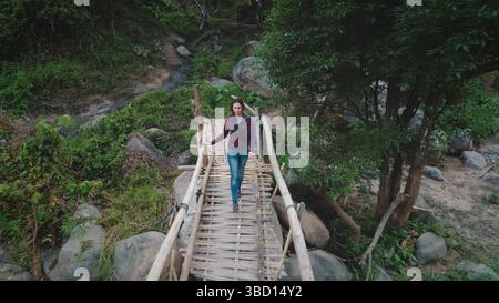 Luftaufnahmen einer weiblichen Touristen, die auf einer Bambusbrücke über einen kleinen Bach in einem tropischen Wald spazieren geht und die Ruhe der Natur genießt Stockfoto