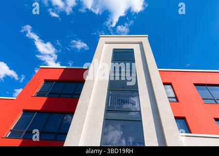Flacher Blick auf ein modernes Gebäude mit roten und weißen Wänden und großen Glasfenstern vor einem leuchtend blauen Himmel. Stockfoto