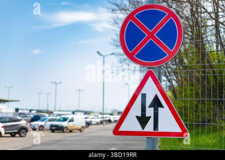 Straßenschilder, die auf einem Zaun in der Nähe eines belebten Parkplatzes unter klarem Himmel hinweisen, dass kein Parkplatz und Zweiwege-Verkehr vorhanden sind. Stockfoto