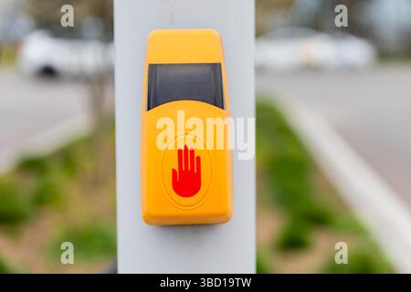 Gelbe Fußgängertaste mit rotem Handsymbol an einem Pfosten neben einer Straße. Stockfoto