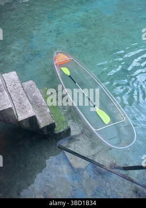 Klares Kajak mit gelben Paddeln, die auf türkisfarbenem Wasser neben Steintreppen schwimmen – ideal für Reisen, Abenteuer und Ökotourismus. Stockfoto