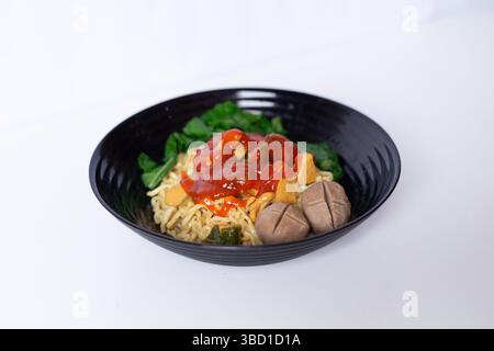 Indonesisches Mie Ayam mit Fleischbällchen und Gemüse serviert auf schwarzer Schüssel. Lecker und herzhaft. Nahaufnahme Stockfoto