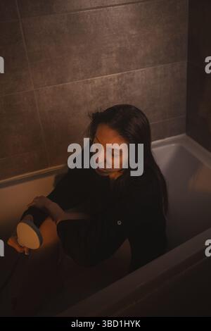 Verärgerte Frau, die mit Armen um die Beine in der Wanne sitzt. Stockfoto
