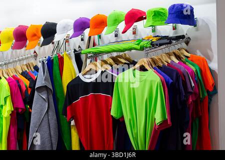 Mehrfarbige T-Shirts und Baseballmützen am Fenster eines Sportgeschäfts. Verkauf Stockfoto