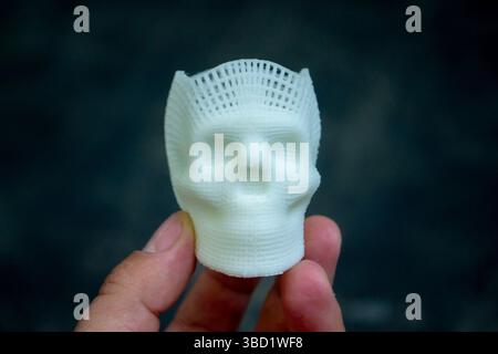 Person, die in den Fingern der Hand hält kleiner weißer Prototyp des menschlichen Schädels 3D gedruckt aus geschmolzenem Kunststoff auf schwarzem Hintergrund. Dreidimensionales Modell. Additive Technologie. Moderne neue Druckindustrie. Stockfoto