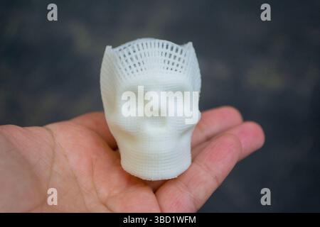 Person, die in den Fingern der Hand hält kleiner weißer Prototyp des menschlichen Schädels 3D gedruckt aus geschmolzenem Kunststoff auf schwarzem Hintergrund. Dreidimensionales Modell. Additive Technologie. Moderne neue Druckindustrie. Stockfoto