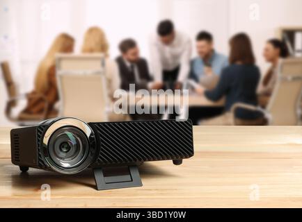 Moderner Videoprojektor auf Holztisch und Personen, die im Konferenzraum arbeiten, selektiver Fokus Stockfoto