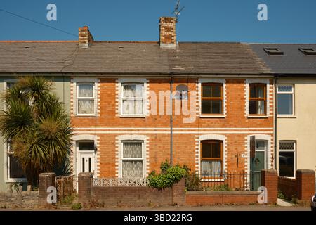 Traditionelle Terrassenhäuser aus rotem Backstein mit weißen Steinverkleidungen in Penarth, Südwales, an einem sonnigen Tag mit klarem blauem Himmel und kleinen Vorgärten. Stockfoto