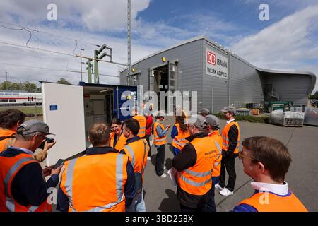 22. Mai 2025, Sachsen, Leipzig: Journalisten, Mitarbeiter und Gäste der Deutschen Bahn stehen vor dem neuen Stromspeicher des ICE-Werks Leipzig. Das sogenannte Second-Life-Batteriespeichersystem besteht aus alten Elektroautos, die über das firmeneigene Solarsystem aufgeladen werden. Die Solaranlage und der Batteriespeicher könnten rund ein Viertel des Strombedarfs des Leipziger EISWERKES decken. Durch das Pilotprojekt würden jährlich rund 85.000 Euro an Energiekosten eingespart. Der nächste Schritt besteht darin, das Instandhaltungswerk in Kassel mit einer Second-Life-Batterie auszustatten Stockfoto