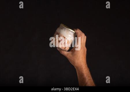 Die männliche Hand hält ein Glas mit hausgemachtem, geschlossenem Fleisch, das in Würfel geschnitten ist Stockfoto
