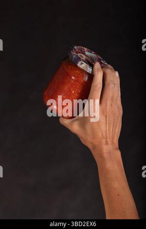 Die männliche Hand hält ein Glas mit hausgemachter Orangengemüsesauce Stockfoto