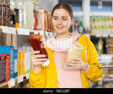 Eine junge Frau, die im Laden Soßen auswählt Stockfoto