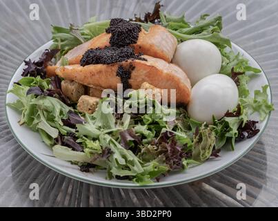 Hausgemachter Salat mit gegrillten Lachsfilets, gekochtem Ei und Croutons auf dem Teller mit Kaviar. Einfaches, aber sehr leckeres Gericht, verwenden Sie es als Hintergrundbild, POS Stockfoto
