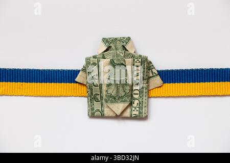 Ukrainisches Flaggenband und Dollarschein in Form eines Hemdes auf weißem Hintergrund, Wirtschaft und Finanzen Stockfoto