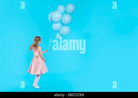 Mädchen in rosa Kleid mit Ballons, die auf blauem Hintergrund mit Kopierraum laufen Stockfoto