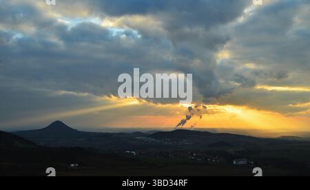 Sonnenstrahlen durchbrechen die Sonnenuntergangswolken über Kraftwerk und Landschaft Stockfoto